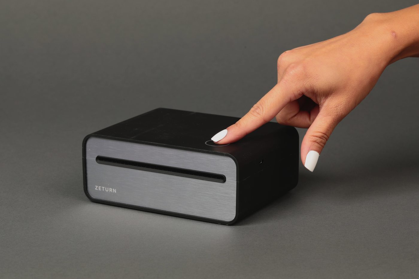 A finger pressing the single button on top of the Zeturn printer