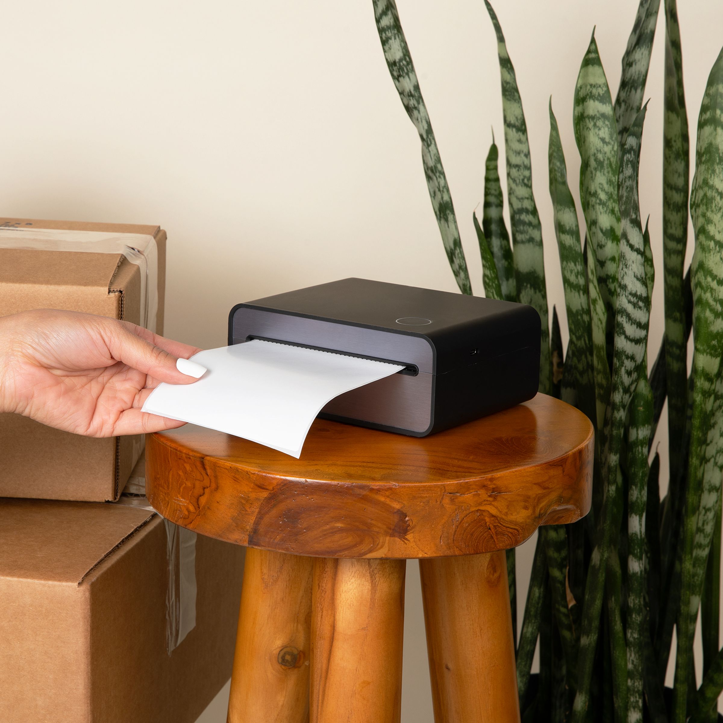 A hand pulling a freshly printed shipping label from the Zeturn printer, beside packed boxes